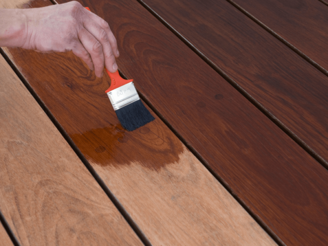 Person using a paintbrush to stain a fence